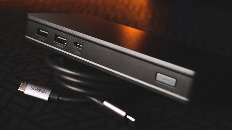 USB-C cable connected to a portable power bank with multiple ports against a dark surface with warm backlighting.