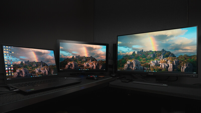Three displays showing identical landscape photographs with mountains, castles, and dramatic sky with rainbow.