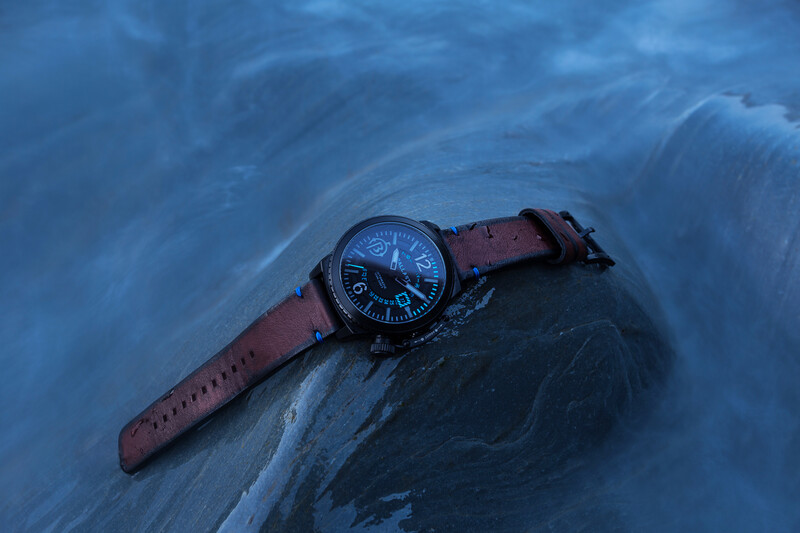 Watch with brown leather strap resting on a wet rock surface with flowing water.
