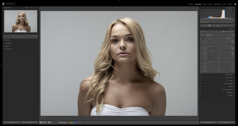 Portrait of a woman with long blonde wavy hair wearing a white strapless top against a neutral gray background.