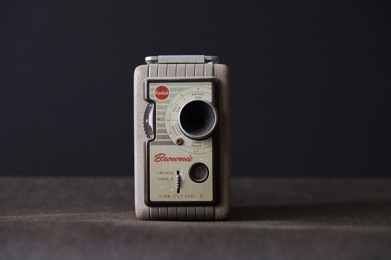 Vintage Brownie movie camera with cream-colored plastic body and metal accents, positioned upright against a dark background.