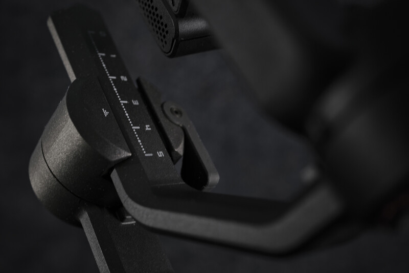 Close-up of a camera gimbal's control handle and adjustment dial against a dark background.