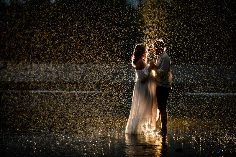 Couple embracing in heavy rain with warm backlighting creating a golden glow around their silhouettes.