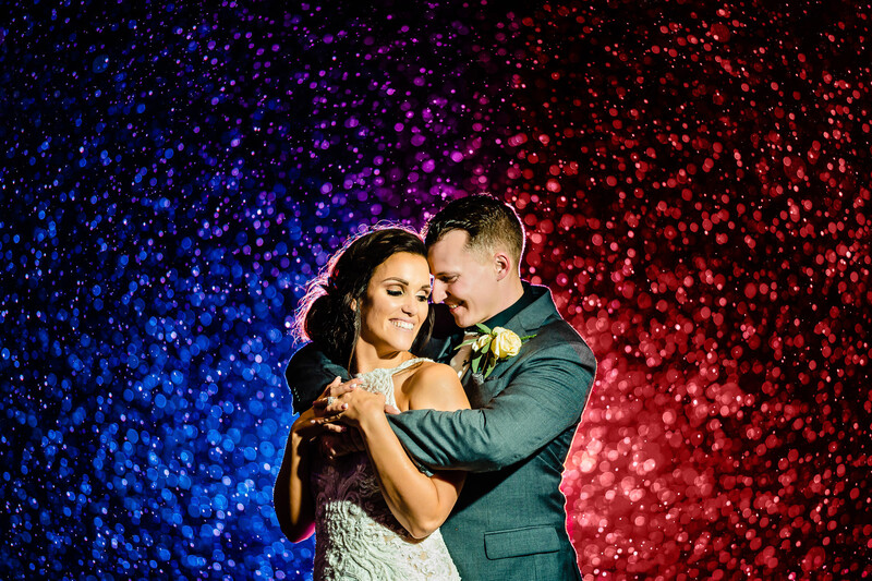 Couple dancing together against a vibrant gradient backdrop of blue, purple, and red bokeh lights.