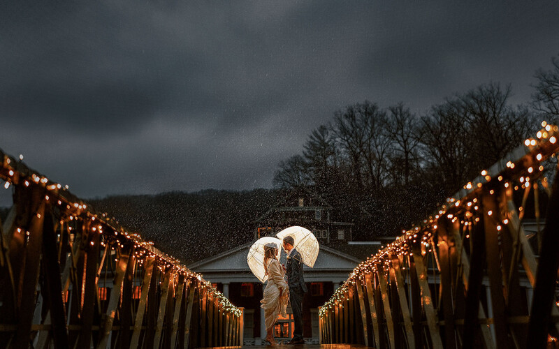 Couple with white umbrella standing in symmetrical corridor of lit candles during overcast weather.