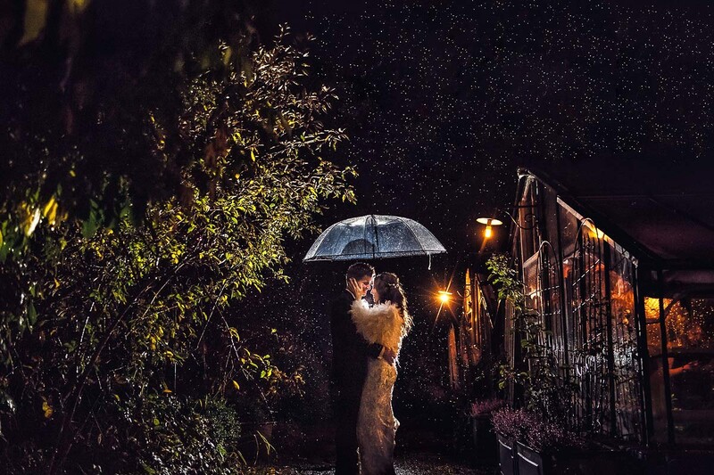 Couple with umbrella in heavy rain at night, illuminated by warm ambient lighting.