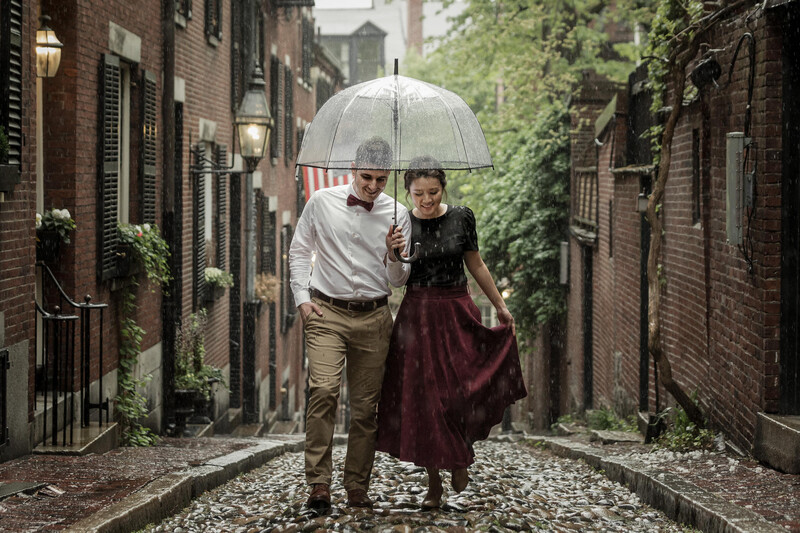 Couple walking through a narrow brick alley in the rain, sharing a clear umbrella.