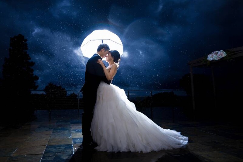 Couple kissing under a luminous moon on a rooftop at night, bride in flowing white gown.