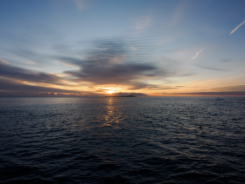 Golden sunset reflected on calm ocean water with clouds illuminated by warm light.