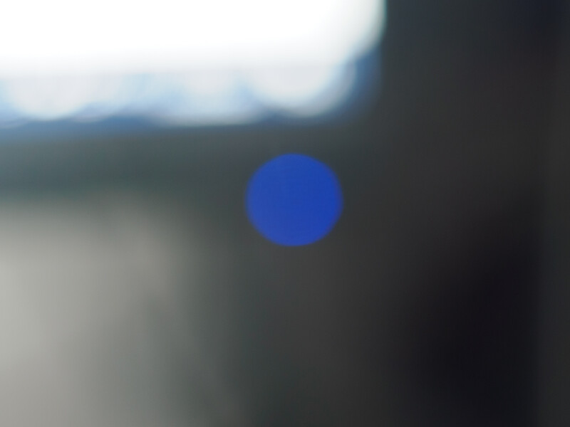 Bright blue circle floating against a blurred landscape with dark foreground and overcast sky.