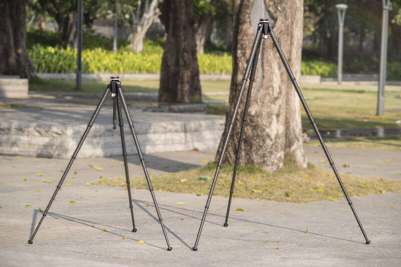 Two tripods of different sizes set up on pavement in a park, with trees and grass visible in the background.