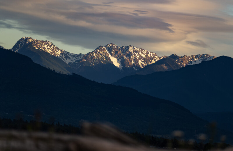 Snow-capped mountain range silhouetted against golden sunset sky with layered ridges in foreground.