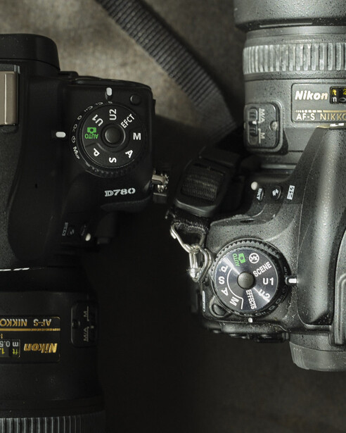 Overhead view of professional camera equipment including a Nikon DSLR body with mode dial visible, telephoto lens, flash unit, and cable on neutral background.