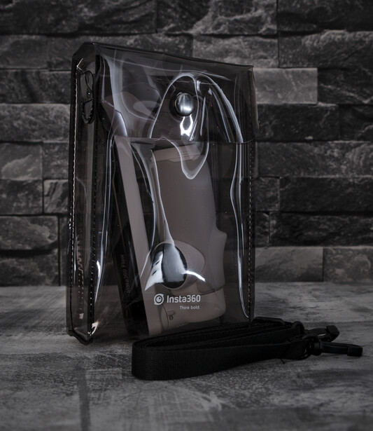 Transparent camera equipment case standing upright on dark tile flooring against a brick wall backdrop.
