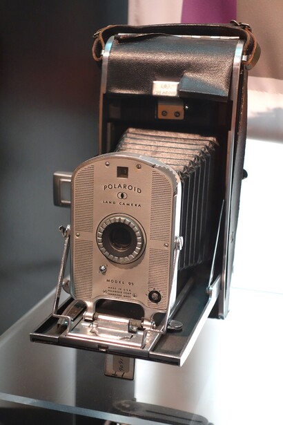 Vintage folding camera with bellows extended, showing tan body and mechanical controls on dark display surface.