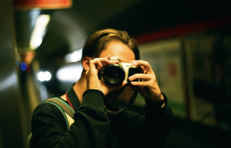 Photographer holding a compact camera up to their face at night, captured in a self-portrait mirror reflection.