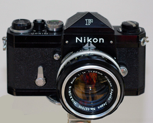Black Nikon F camera with chrome-ringed Nikkor lens mounted on gray background.