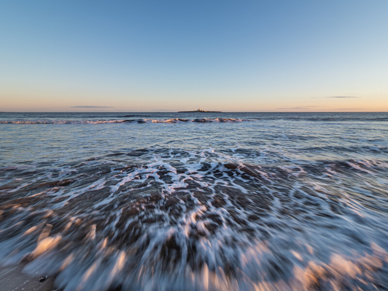 Ocean waves washing onto sandy beach at twilight with motion blur effect.