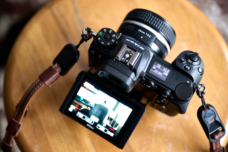 Two mirrorless cameras with lenses and an external monitor on a wooden surface.