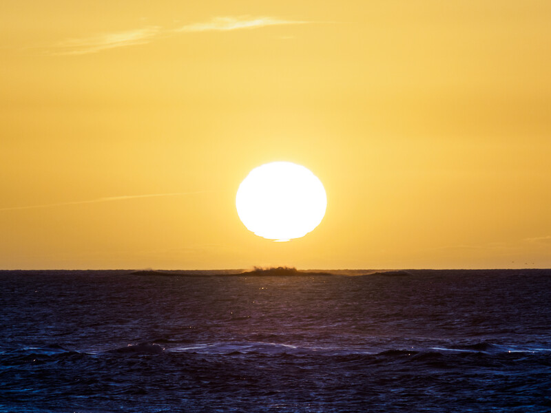 Large bright sun setting on horizon over dark ocean waters under golden sky.