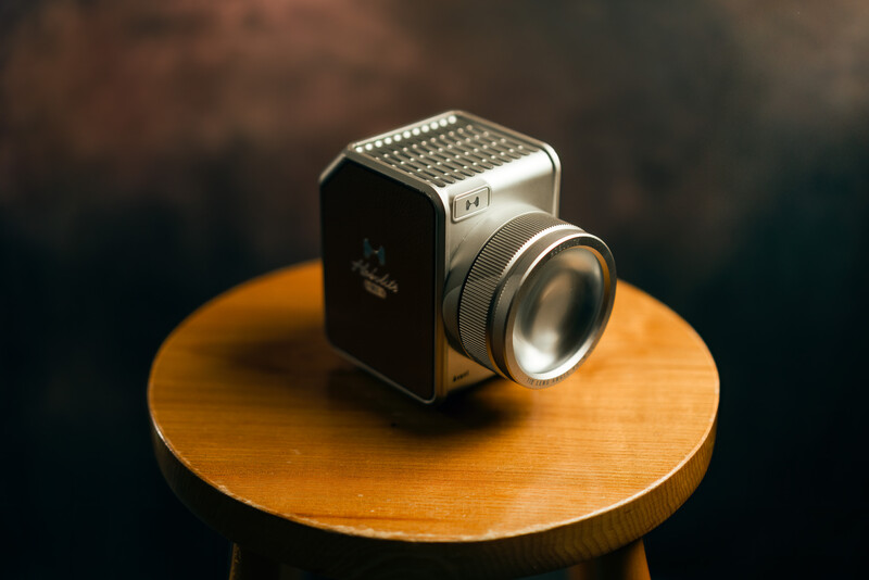 Vintage film camera with square body and large lens mounted on wooden circular platform.