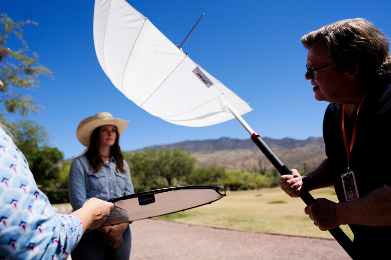 Three people demonstrating reflector use outdoors in bright sunlight with mountains in background.