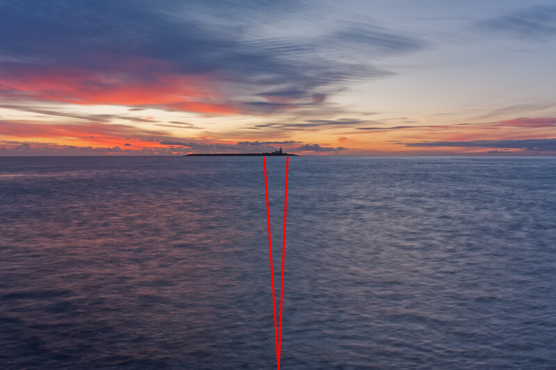 Two vertical red lines extending into calm water under a dramatic sunset sky.