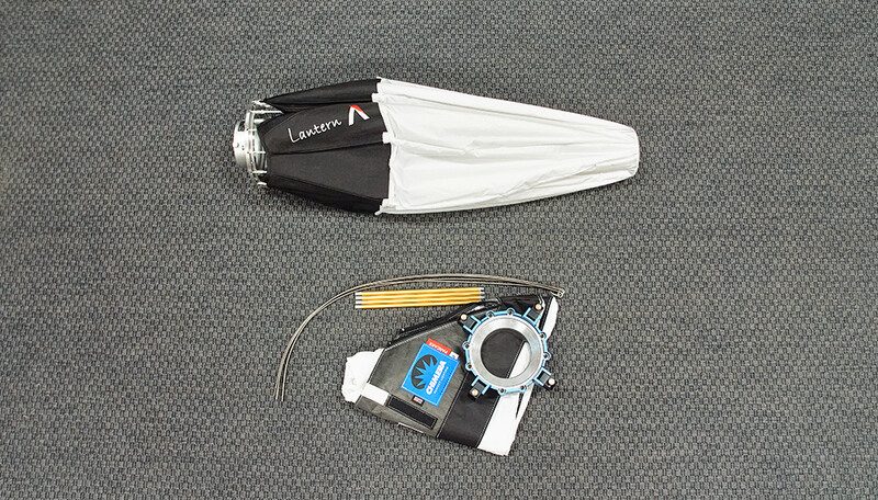 Overhead view of a softbox with white diffusion material and a camera flash setup with accessories on gray fabric.