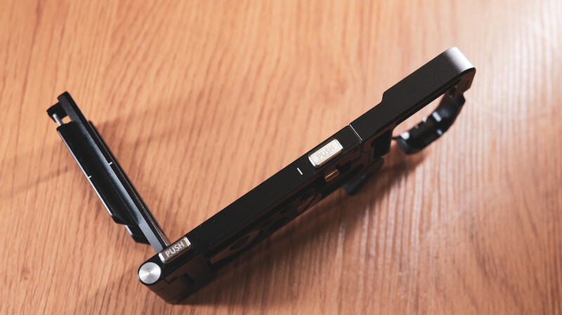 Black camera strap with metal attachment points on wooden surface.