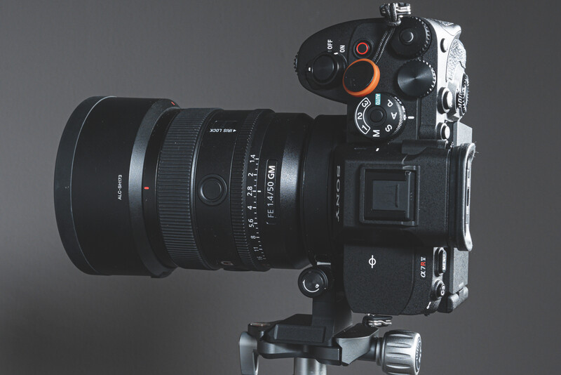Mirrorless camera with attached telephoto lens mounted on tripod against gray background.