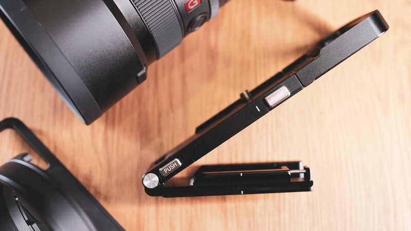 Black camera slider with extending arm positioned on wooden surface next to camera lens and body.