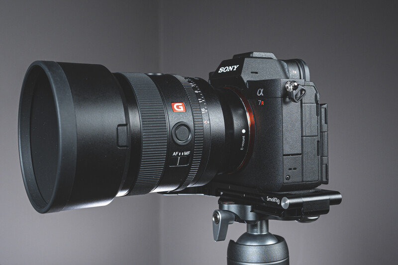 Sony mirrorless camera with telephoto lens mounted on tripod head against gray background.