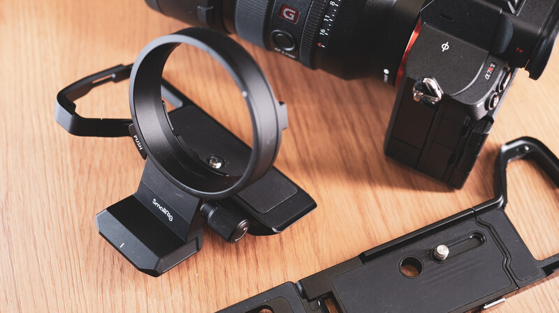 Camera lens adapter mounted on a black tripod stand next to a digital camera body on a wooden surface.