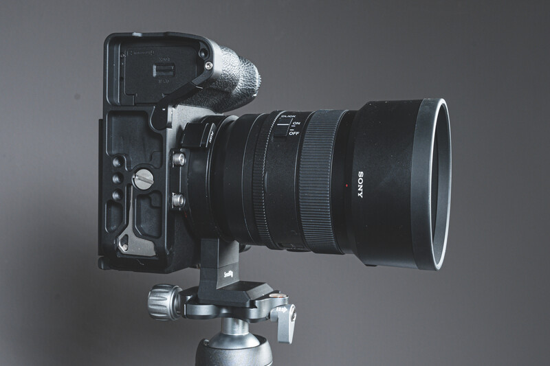 Mirrorless camera with telephoto lens mounted on a ball head tripod against a gray background.