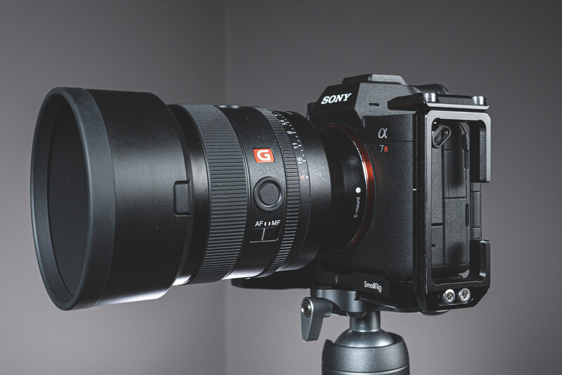 Sony Alpha mirrorless camera with telephoto lens mounted on tripod ball head against gray backdrop.