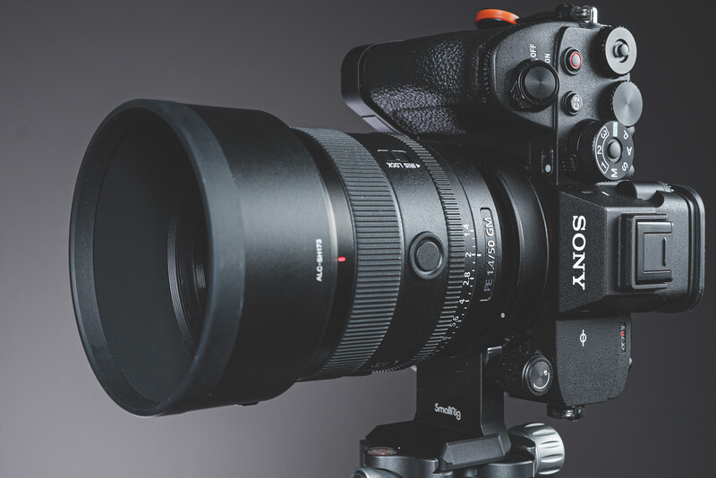 Sony mirrorless camera with telephoto lens mounted on tripod head against gray background.