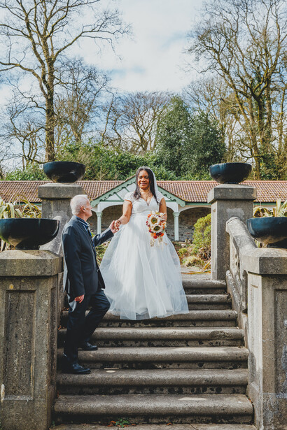 Bride and groom on stone steps in a garden setting with bare trees in background.