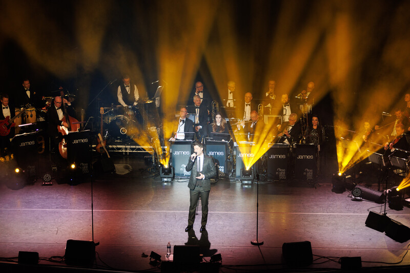 Soloist performing center stage under dramatic golden and purple uplighting with full orchestra and choir behind.