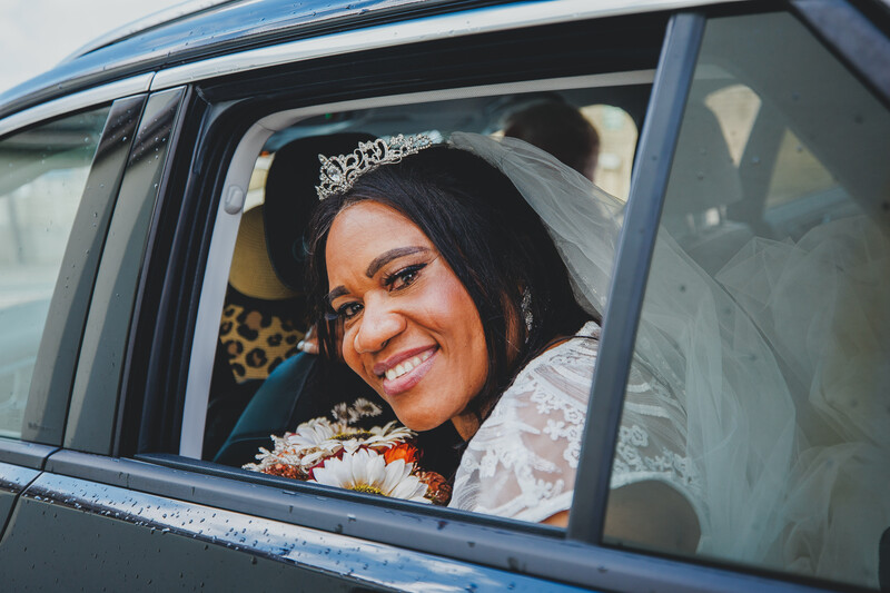 Bride in white lace veil and tiara smiling through car window on wedding day.