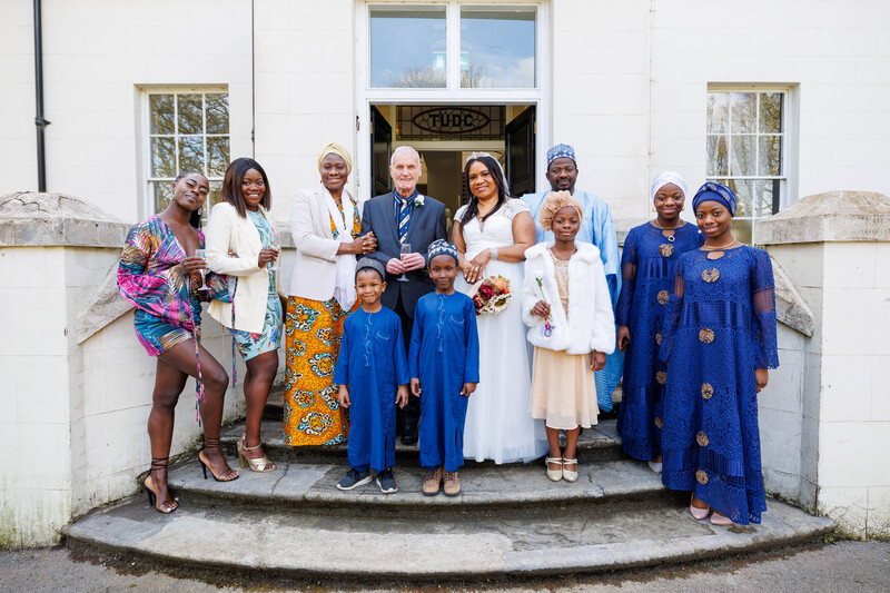 Group of people in colorful traditional and formal attire standing on steps outside a white building.