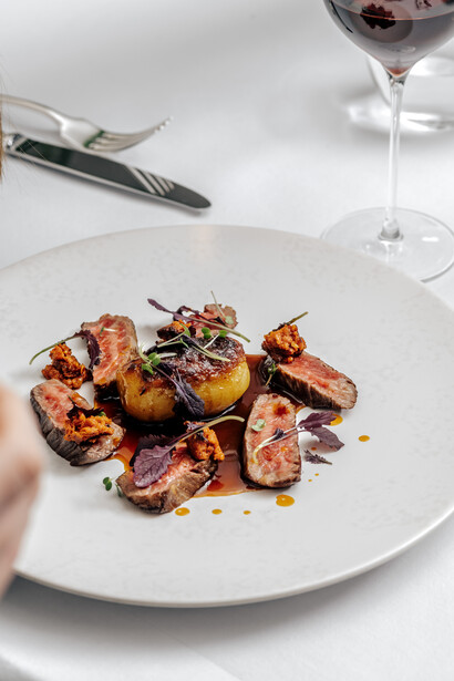 Plated seared scallops and duck breast with dark glaze and microgreens on white dish.