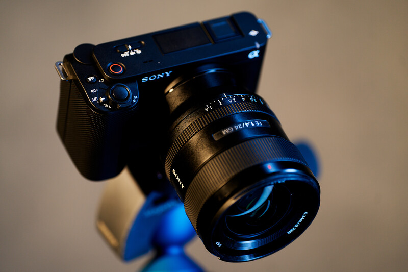 Sony mirrorless camera with prime lens mounted, positioned on blue tripod head against neutral background.