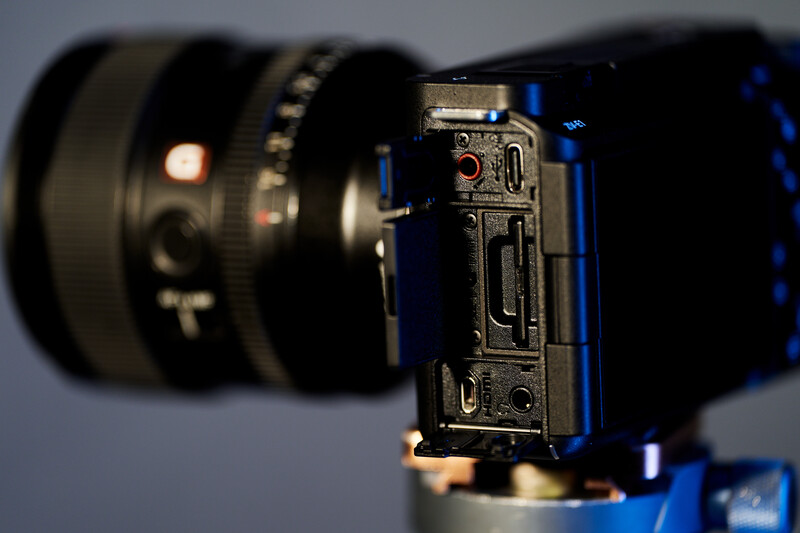 Camera body with mounted lens viewed from the side, showing ports and controls in sharp focus with blurred lens in background.