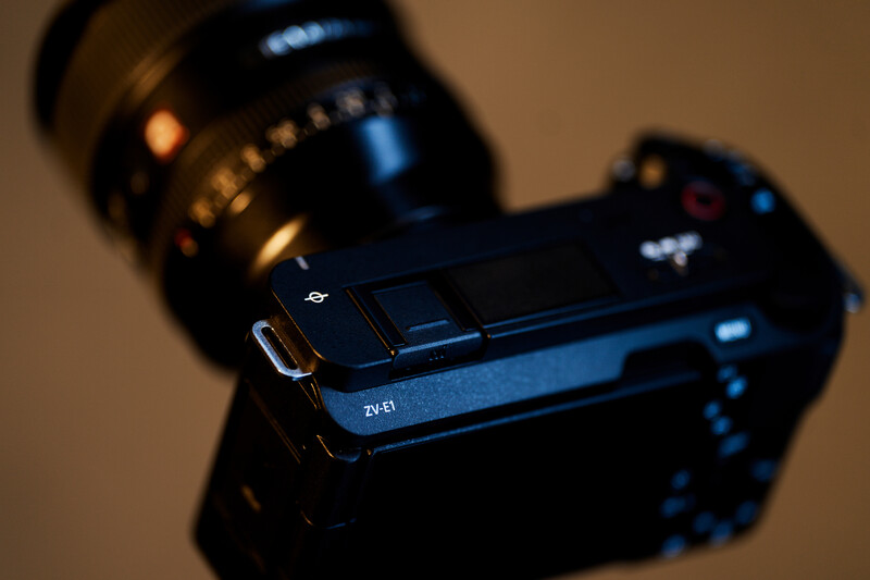 Close-up of a compact video camera's control panel and lens in warm studio lighting.