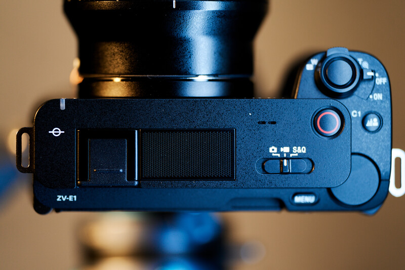 Top-down view of a blue mirrorless camera with attached lens, showing the body's right side and control buttons.