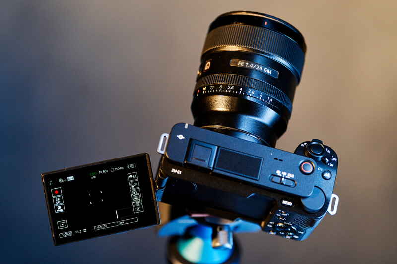 Sony mirrorless camera with articulating screen and mounted prime lens against neutral background.