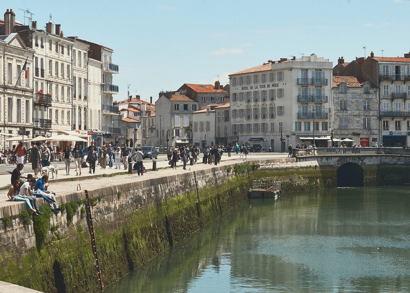 Waterfront promenade with stone wall, river, and European architecture under clear sky.