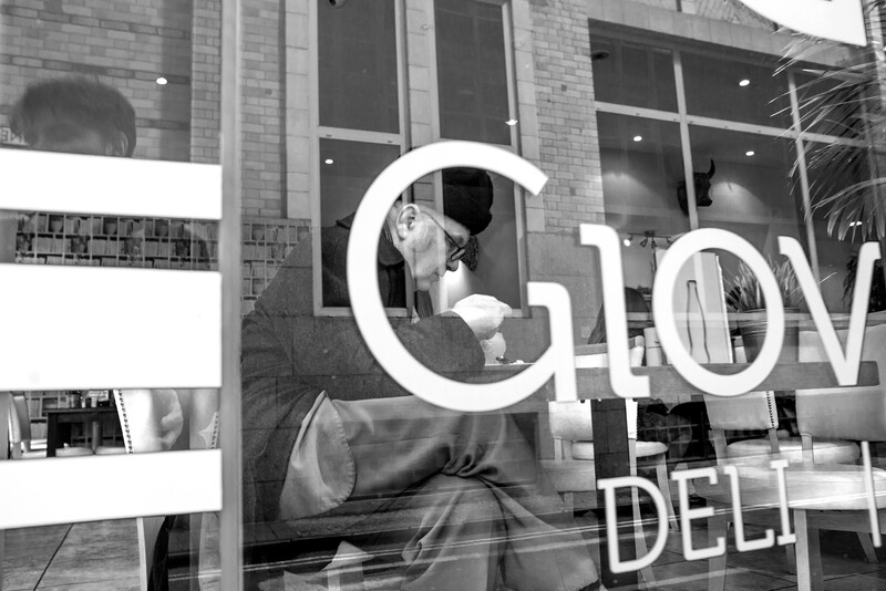 Black and white storefront window with large white letters and reflections of buildings and people.