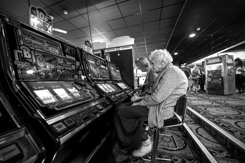 Elderly woman playing a slot machine in a casino, shot in black and white.