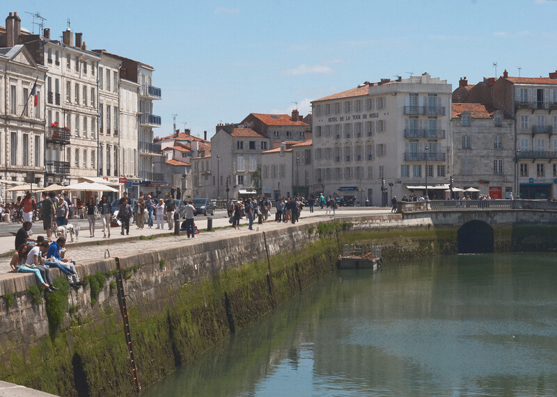 European waterfront promenade lined with classical buildings and pedestrians walking along a stone quay.